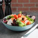 A bowl of salad with vegetables and meat in a blue crackle melamine bowl.