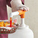 A gloved hand using a Tablecraft WideMouth Maxi Pelican Pump to pour ketchup onto a basket of fries.