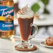 A glass of coffee with Torani Sugar-Free Caramel Flavoring Syrup and whipped cream next to a cookie.
