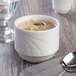 A white Libbey porcelain bowl of noodle soup with a spoon.