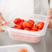 A person holding a Cambro translucent polypropylene food pan with tomatoes in it.
