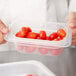 A person holding a Cambro translucent plastic food pan filled with cherry tomatoes.