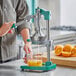A person using the Garde manual citrus juicer to make orange juice with a measuring cup full of orange juice and a cut orange nearby.