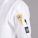 A person wearing a white Chef Revival chef coat with a yellow device in the pocket.