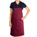 A woman wearing a burgundy Chef Revival bib apron standing in a professional kitchen.