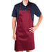 A man wearing a burgundy Chef Revival bib apron in a professional kitchen.