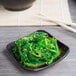 A Libbey square stoneware dip dish with green seaweed on a table.
