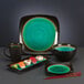 A black Libbey stoneware bowl filled with green liquid on a table with sushi.