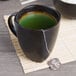 A Libbey stoneware mug filled with green tea and a tea bag on the side.