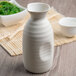 A white Libbey stoneware sake bottle on a table with a bowl of food.