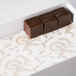 A white 3-ply Glassine pad with gold floral pattern holding chocolate cubes.