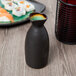 A black Libbey stoneware sake bottle filled with green liquid on a table with sushi.