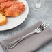 A Bon Chef stainless steel dinner fork on a napkin next to a plate of pasta.