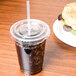 A plastic cup with a clear Eco-Products straw in it and a brown drink on a table with a sandwich.