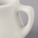 A close-up of a white Tuxton creamer on a white surface.