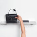 A hand holding a black purse on a Bobrick stainless steel wall shelf.