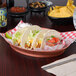 HS Inc. paprika oval deli server holding a plate of tacos on a table.