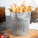 A metal bucket of French fries with ketchup on a wood surface.
