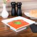 A CAC Citysquare white porcelain bowl filled with red tomato soup with a spoon on a table.