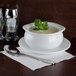 A white bowl of Silver Skillet cream of mushroom soup with a green leaf on top on a table with a spoon on a napkin.