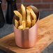 An American Metalcraft copper cup filled with french fries on a wooden surface.