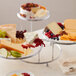 A Wilton three-tiered display stand with trays of fruit and cheese on a table.