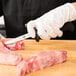 A person using a Victorinox poultry boning knife to cut raw meat on a cutting board.