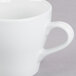 A close-up of a white Tuxton Europa cappuccino mug with a handle.