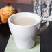 A close-up of a Tuxton white porcelain cappuccino mug filled with coffee on a table with a muffin.