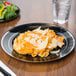 A Fineline black plastic plate with silver bands holding pasta with cheese and salad next to a glass of water.