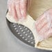 A person in plastic gloves making dough on an American Metalcraft Super Perforated Hard Coat Anodized Aluminum Pizza Pan.