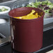 A red Cambro crock filled with yellow peppers on a counter.