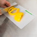 A person cutting a yellow bell pepper on a WebstaurantStore flexible cutting board.