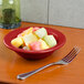 A Tuxton cayenne Colorado china bowl filled with sliced fruit on a table next to a fork.
