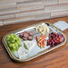 A Vollrath rectangular metal catering tray with gold trim holding cheese and grapes on a table at a catering event.