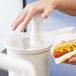 A person using a Cambro clear plastic lid to dispense a hot dog condiment.