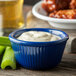 A Carlisle cobalt blue fluted ramekin filled with white sauce on a table with chicken wings and celery.