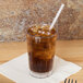 A Cambro clear plastic tumbler filled with iced coffee on a table.