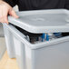 A hand opening a Rubbermaid tote box lid on a plastic container.
