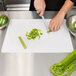 A person cutting vegetables on a Tablecraft white flexible cutting board.