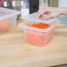 A hand using a Cambro translucent plastic container lid to cover a container of carrots.