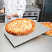 A chef holding a pizza on an American Metalcraft aluminum pizza peel.