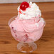 A clear Fineline Flairware plastic dessert cup filled with pink ice cream and a cherry on top.