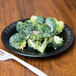 A Dart black foam plate with a piece of broccoli on it, next to a fork on a wood table.