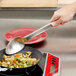 A person using a Vollrath Jacob's Pride stainless steel spoon to stir a pan of food.