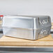A silver aluminum Vollrath roaster pan on a wooden cutting board.