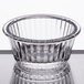 A clear fluted plastic ramekin with a rim on a table.