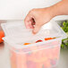 A hand using a Cambro translucent plastic lid to cover a container of peppers.