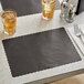 A table set with a Choice black scalloped paper placemat and two glasses of liquid.