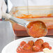 A person using a Vollrath Ivory Solid Oval Spoodle to serve meatballs with red sauce.